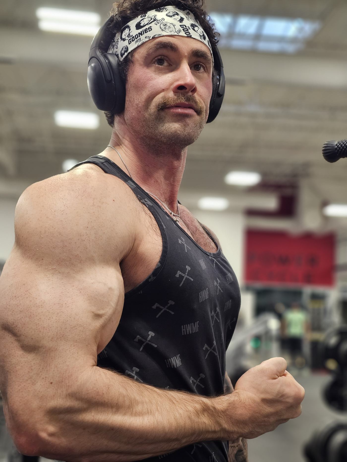 Logan in the gym, flexing his arm in a black tank top