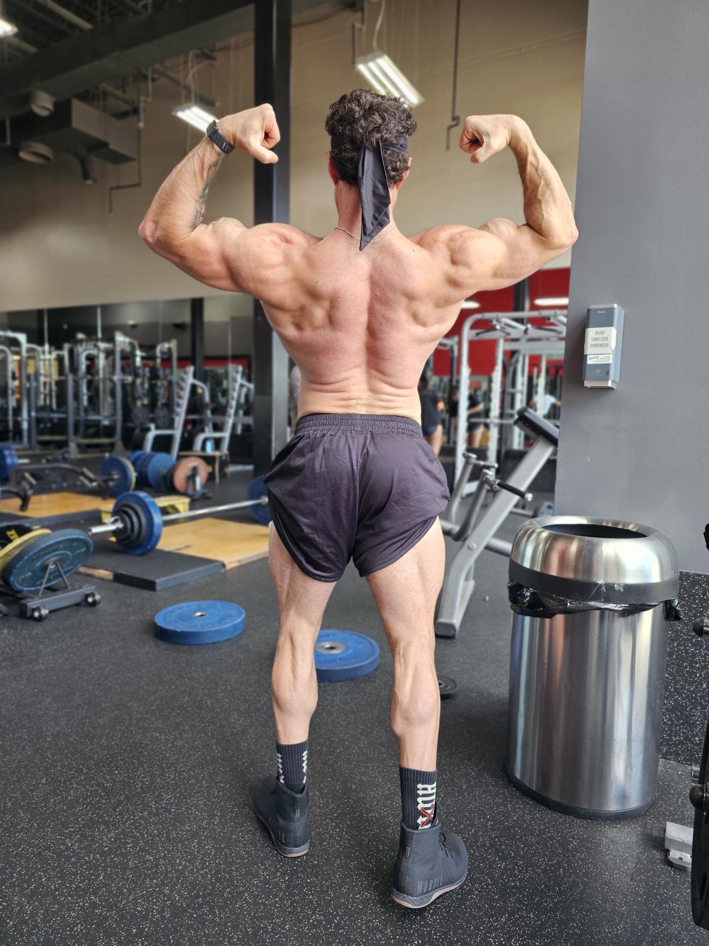 Logan from behind, hitting a back double biceps pose in the gym